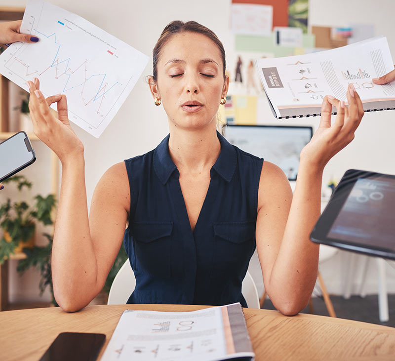 אישה יושבת במשרד מול שולחן העבודה ועושה עם הידיים תנועה מדיטציה