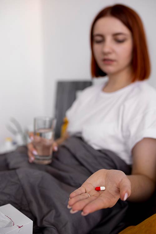 אישה יושבת זקופה במיטה. ביד אחת מחזיקה כוס מים וביד השניה בפוקוס מחזיקה כדור לבן אדום